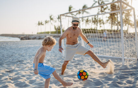 Father with his son plaing football on the beach.