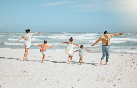 Playful mixed race family with three children running on the beach with arms outstretched. A big family spending time and enjoying holiday by the sea